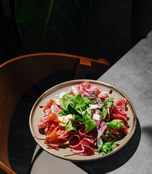 Etler ve taze yeşillikler içeren canlı bir salata nötr bir tabakta düzenlenir. Tabak, minimalist dekor arkaplanlı desenli bir yüzeye yerleştiriliyor..