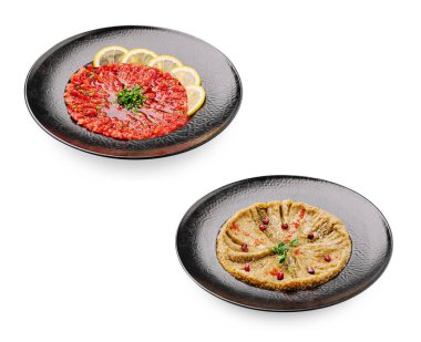 İki lezzetli geleneksel yemek siyah tabaklar üzerinde güzelce düzenlenmiştir. Biri canlı kırmızı malzemeler ve limon dilimleri içerirken, diğeri süslemeli kremalı dokular sergiliyor..