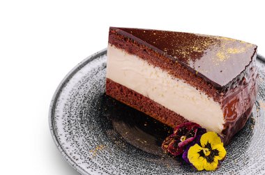 Zengin çikolatalı pasta dilimleri, kremalı dolgular ve parlak bir üst. Renkli, yenilebilir çiçeklerle süslenmiş, dokulu bir tabağa oturmuş, tatlı aşıklarını davet ediyor..