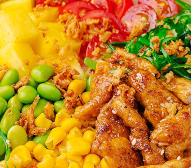 Izgara tavuk, taze yeşillikler, mısır, edamame, domates ve ananasla dolu canlı bir kase. Bu yemek sağlıklı ve lezzetlerle dolu. Öğle yemeği vakti doyurucu bir yemek için mükemmel..