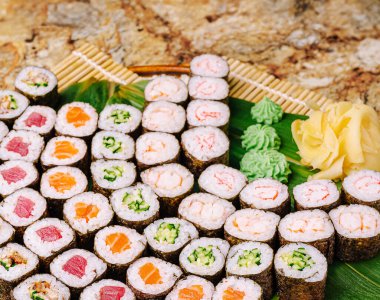 Renkli tabakta ton balığı, somon ve sebze seçenekleri de dahil olmak üzere bir dizi suşi rulosu yer alıyor. Suşi wasabi ve zencefil turşusuyla süslenir ve canlı bir yemek oluşturur..