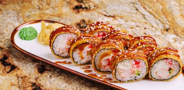 Suşi rulolarının lezzetli bir çeşidi beyaz bir tabakta güzelce düzenlenir. Ekmekler canlı renkler ve dokular içeriyor. Taze deniz ürünleri ve süslemeler sergileniyor. Paylaşım için mükemmel..