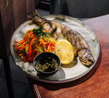 Güzel bir kaplanmış ızgara balık otlarla kaplı gümüş bir tabakta rengarenk sebzeler ve limon diliminin yanında oturur..