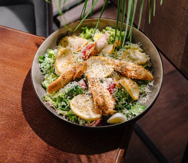 Canlı bir salatada sebzeler, çıtır tavuk ve renkli sebzeler bulunur. Ahşap bir yüzeyde, derin bir kasede, öğle veya akşam yemeği için sağlıklı bir yemek fikri sunuyor..