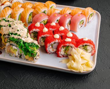 Düzenli bir şekilde sıralanmış canlı bir suşi tabağı. Önemli noktalar arasında somon, ton balığı ve soslu yengeç ruloları ve süslemeler yer alıyor. Taze tatları paylaşmak ve zevk almak için ideal..