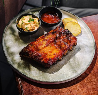 Kremalı lahana salatası ve keskin sosla servis edilen leziz barbekü kaburgaları. Ortam sıcak ve davetkar, doyurucu bir yemek için mükemmel..