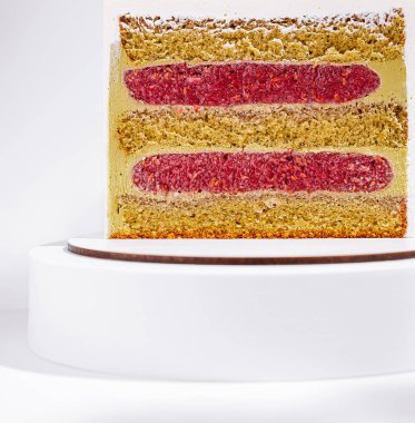 Güzel hazırlanmış bir pasta beyaz bir kaidede oturur. Sergide ahududu dolgusu ve sarı sünger katmanları, canlı renkler ve net bir kesim yer alıyor..