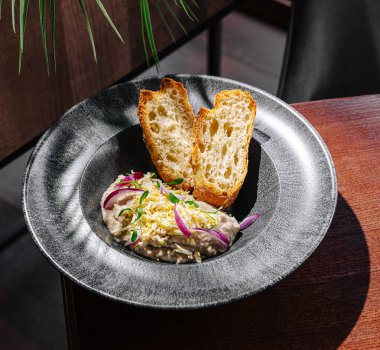 Çok güzel sunulan bir yemek, kremalı, soslu ve iki dilim kızarmış ekmekle servis ediliyor. Ortam modern, koyu ahşap elementler ve yeşil bitki detaylarıyla..