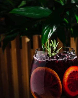 Canlı bir içecek, uzun bir bardakta buzun üzerinde servis edilen dilimlenmiş kan portakalları ve taze otlardan oluşur. Yeşil yapraklar doğal bir zemin sağlar, ferahlatıcı görünümü arttırır..