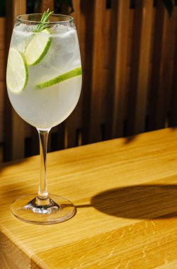 Limon ve salatalık dilimleriyle dolu köpüklü narenciye dolu uzun bir bardak pürüzsüz bir ahşap masada oturur. Ilık aydınlatma sıcak bir atmosfer yaratır..