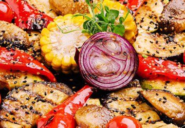 Izgara sebzelerin canlı bir karışımı güzel bir tabakta düzenlenmiştir. Kırmızı biberler, soğanlar, mısırlar ve mantarlar baharatlıdır ve yaz aylarında toplanan tat alma tomurcuklarını tatmaya hazırdır..