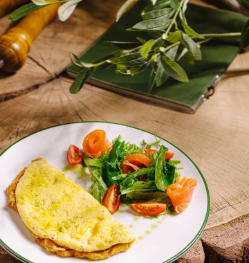 İyi hazırlanmış bir omlet taze yeşilliklerden, kiraz domateslerinden ve füme somon dilimlerinden yapılmış canlı bir salatanın yanında beyaz bir tabakta oturur..