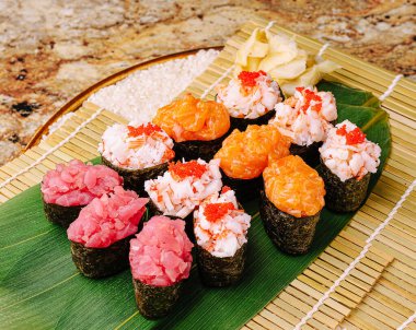 Renkli bir suşi tabağı ton balığı, yengeç ve somon da dahil olmak üzere farklı türde suşi içerir. Suşi zarif bir şekilde bambu bir hasırın üzerinde süslenmiş, canlı bir seçim sergiliyor..