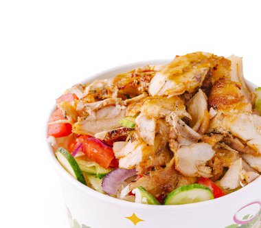 Izgara tavuk, domates ve salatalık da dahil olmak üzere taze sebzelerden oluşan bir yatağın üzerinde renkli bir kasede servis edilir..