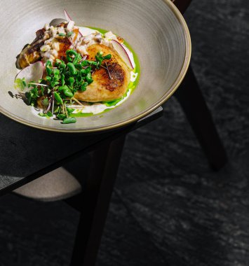 Taze yeşillikler ve hassas soslarla süslenmiş yuvarlak bir tabakta güzel bir şekilde sunulmuş tavuk yemeği servis edilir. Ayar koyu yüzeyi olan minimalist bir tablo içeriyor..