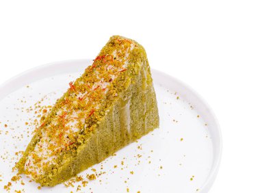 Bir dilim şam fıstıklı kek temiz beyaz bir tabakta oturur. Tatlı safran iplikçikleri ve ezilmiş fıstıklarla kaplı. Bu da davetkar bir görünüm sağlıyor..