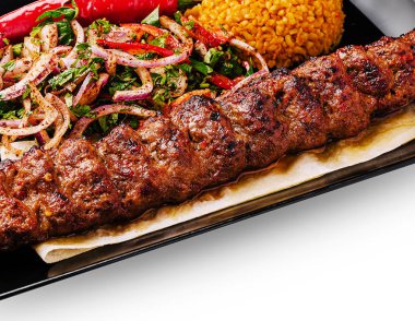 Baharatlı pirinç ve soğan ve biberli renkli salatayla birlikte bir tabağa konmuş yumuşak kebap. Bu yemek Orta Doğu mutfağında popüler olan lezzetlerin bir karışımını sergiliyor..