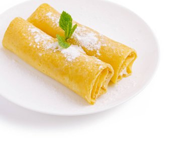 İki altın rengi krep, beyaz bir tabakta, hafifçe pudra şekeri ile tozlanmış ve süslemek için taze bir nane yaprağı ile kaplanmış..