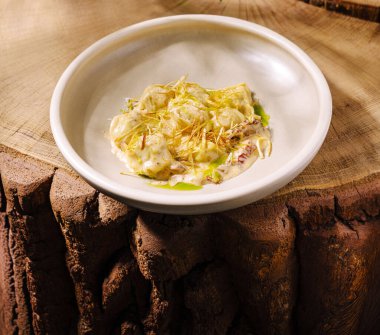 Güzel düzenlenmiş bir tabak, ahşap bir yüzeyde oturur. Tabakta ince altın iplikçiklerle süslenmiş özenle hazırlanmış yemekler var..