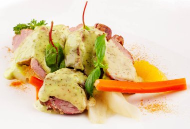 Yumuşak kavrulmuş ördek, taze fesleğenle süslenmiş yeşil bir sosla kaplanır ve lezzetli bir yemek için canlı havuç ve diğer sebzelerle birlikte sunulur..