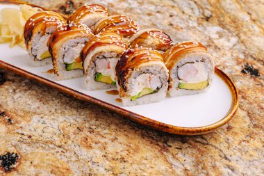 Lezzetli soslu suşi ruloları ve susam tohumları dekoratif bir tabağa konur. İçinde karides, avokado ve baharat gibi taze malzemeler var..