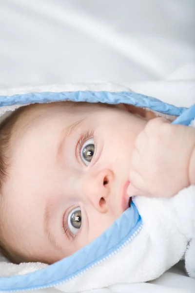 Mooie kleine baby met grote ogen witte handdoek in zijn hand bijten — Stockfoto