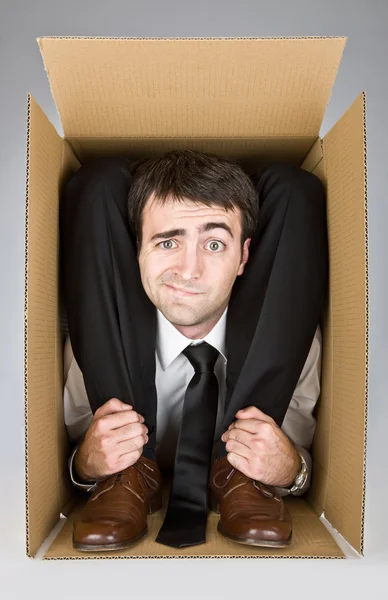 Uomo d'affari flessibile con faccia dubbia in una scatola di cartone — Foto Stock