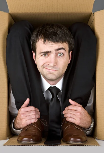 Flexible businessman with doubtful face in a cardboard box — Stock Photo, Image