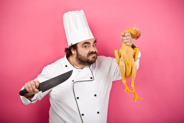 Chef louco e selvagem com faca mostrar frango isolado em rosa — Fotografia de Stock