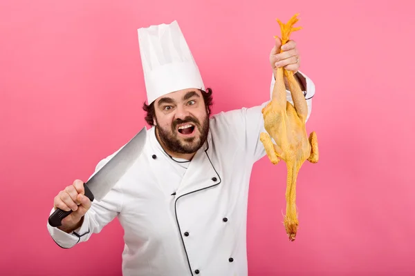Chef louco e selvagem com faca mostrar frango isolado em rosa — Fotografia de Stock