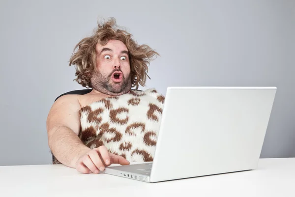 Grappig perplex prehistorische man met laptop — Stockfoto