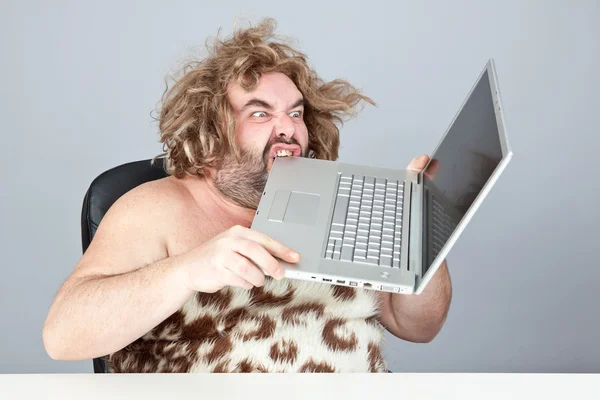 Hungry and angry prehistoric man eat laptop — Stock Photo, Image