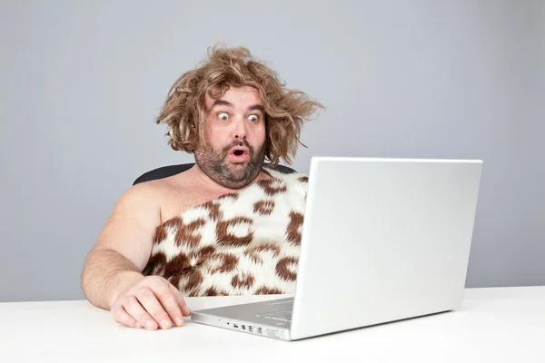 Funny perplex prehistoric man using laptop — Stock Photo, Image