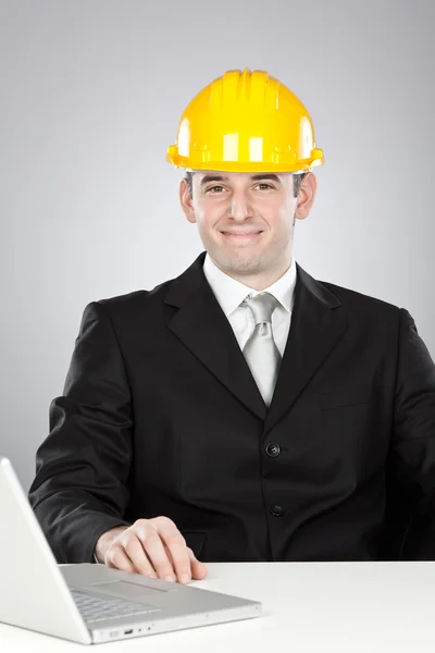 Schön lächelnder Ingenieur mit gelbem Helm und Laptop isoliert auf grau — Stockfoto