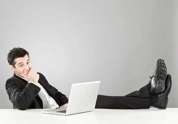 Relaxed happy businessman with laptop at desk isolated on grey — Stock Photo, Image