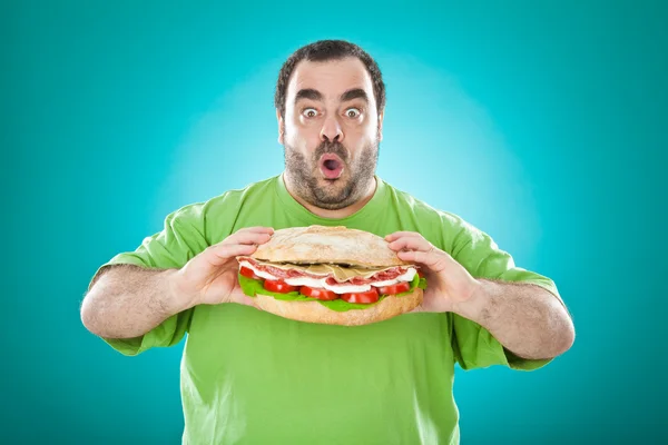 Толстый смешной человек ест огромный сэндвич изолирован на синий — стоковое фото