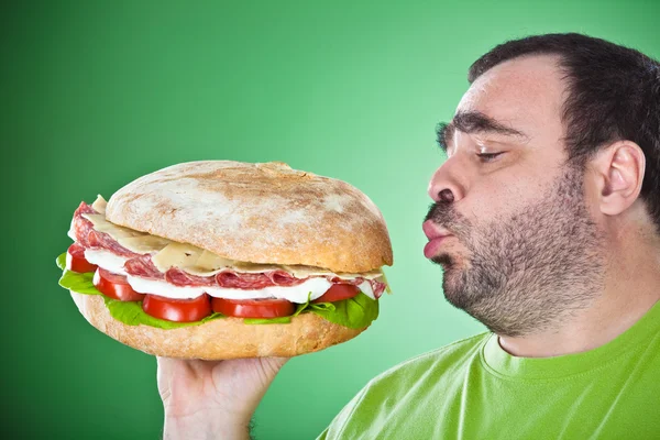 Fat funny man eat a huge sandwich isolated on green — Stock Photo, Image