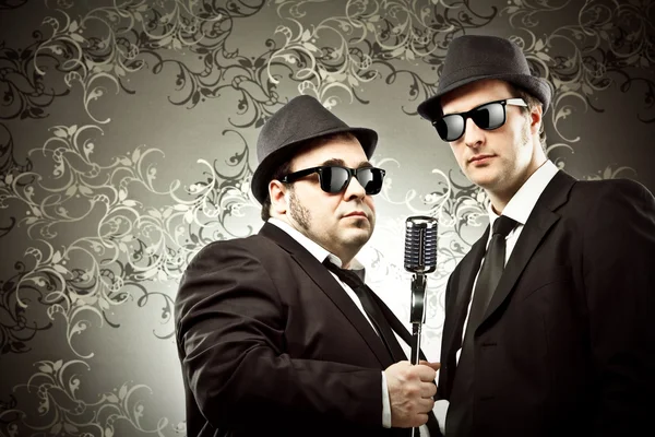 Пара смешных винтажных певцов с портретом микрофона на гобеленовом фоне — стоковое фото