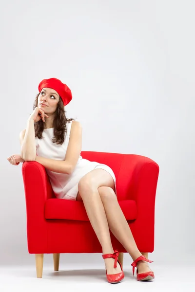 Beautiful smiling woman relaxed on red armchair isolated on grey — Φωτογραφία Αρχείου