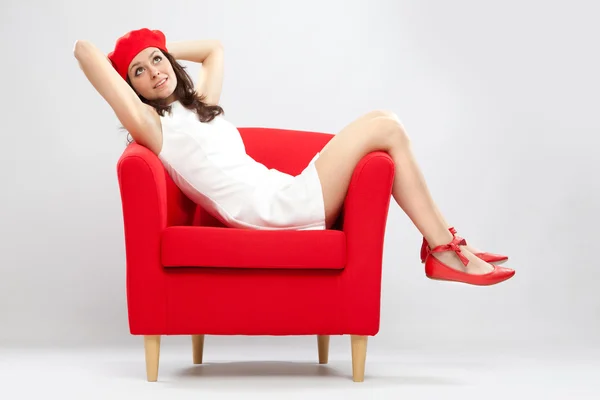 Beautiful smiling woman relaxed on red armchair isolated on grey — Φωτογραφία Αρχείου