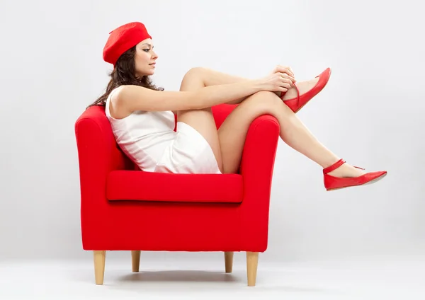 Hermosa mujer sonriente relajada en sillón rojo aislado en gris — Foto de Stock