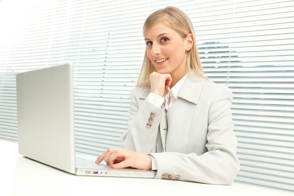 Femme d'affaires blonde souriante avec ordinateur portable près de la fenêtre aveugle vénitienne — Photo