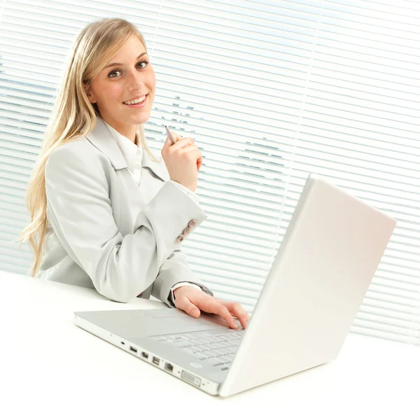 Femme d'affaires blonde souriante avec ordinateur portable près de la fenêtre aveugle vénitienne — Photo