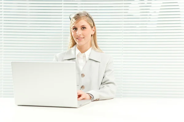 Χαμογελώντας ξανθά επιχειρηματίας με τον φορητό υπολογιστή κοντά ζηλίες, περσίδες παράθυρο — Φωτογραφία Αρχείου
