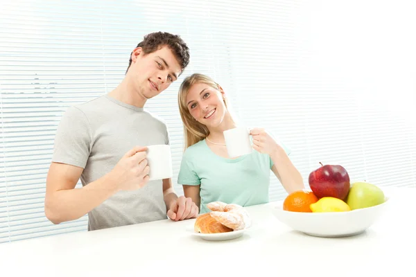 Young casual couple have breakfast with coffee and fruit with venetian blind window