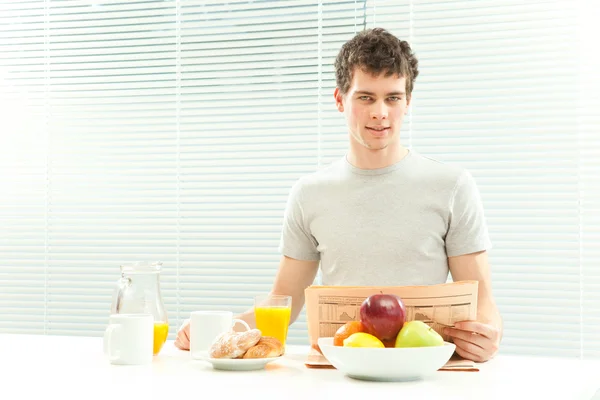 Curly young man have breakfast read newspaper with venetian blind window — Stock Photo, Image