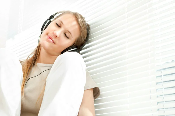 Joven hermosa mujer escuchar música con auriculares en una sala de estar —  Fotos de Stock