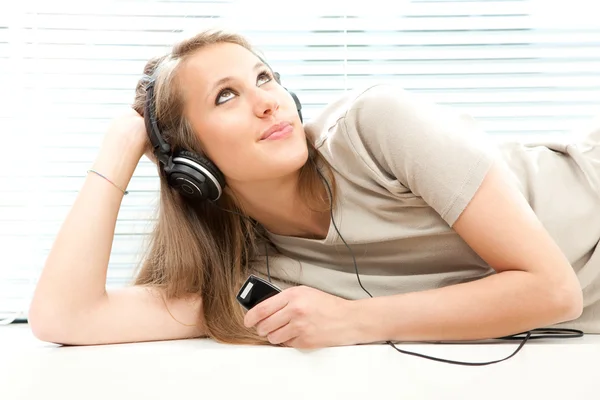 Joven hermosa mujer escuchar música con auriculares en una sala de estar —  Fotos de Stock