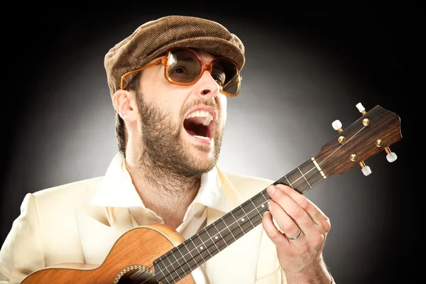 Homem engraçado com óculos jogar ukelele guitarra no fundo preto — Fotografia de Stock