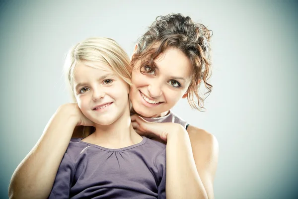 Mooie brunette vrouw met jong blond meisje op grijze achtergrond — Stockfoto